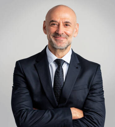 istockphoto-1934523168-612x612 Portrait of caucasian business man looking at camera and smiling. Confident mature male professional is in suit. He is against gray background.